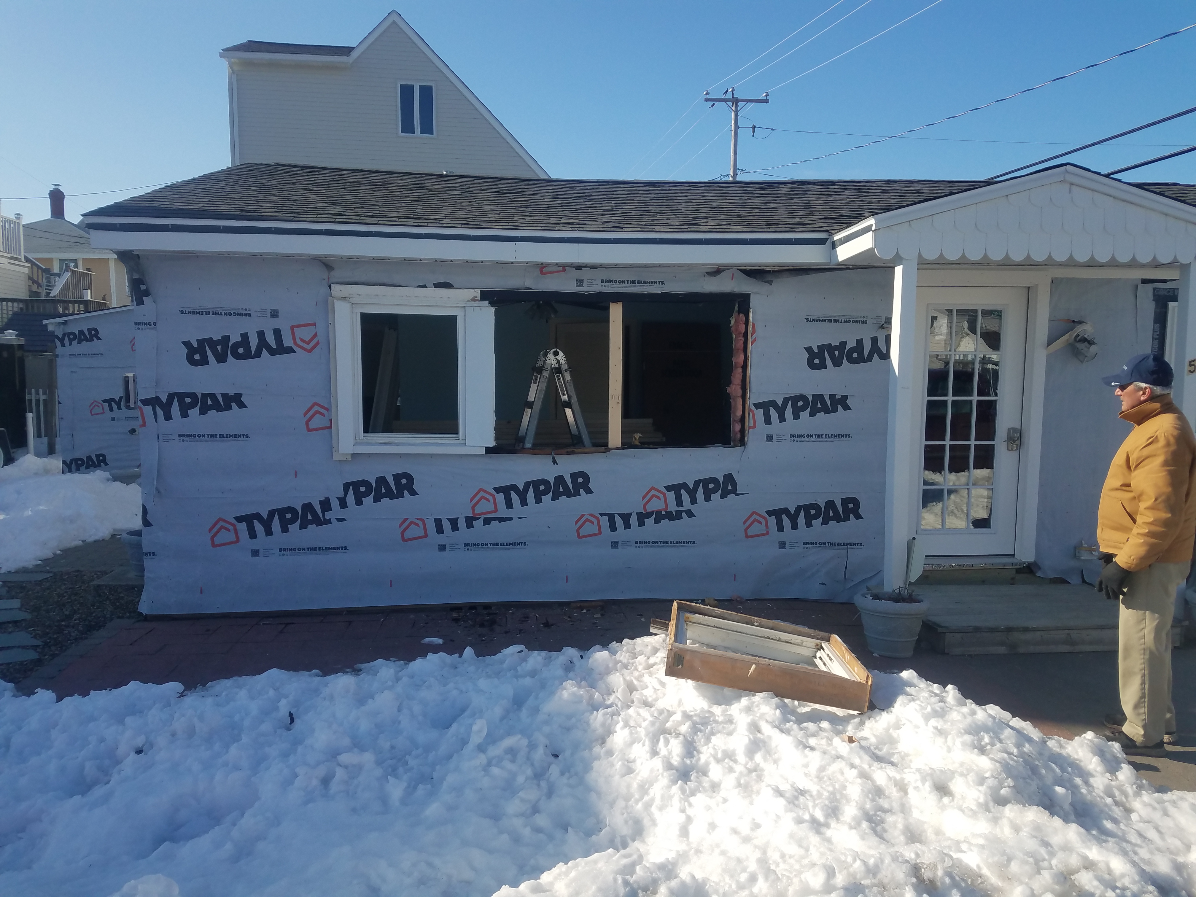 A house wrapped in building paper in the snow with an opening cut for a new door and the old window out in the yard