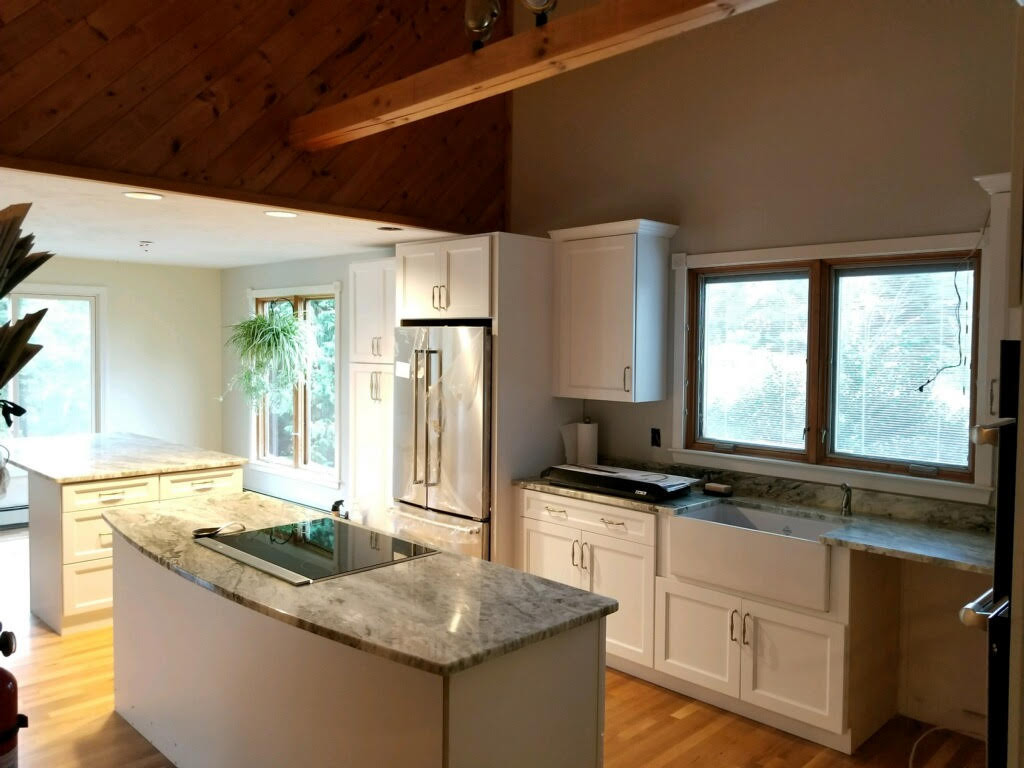 Kitchen with granite island, white cabinets and a farmhouse sink under a pine ceiling