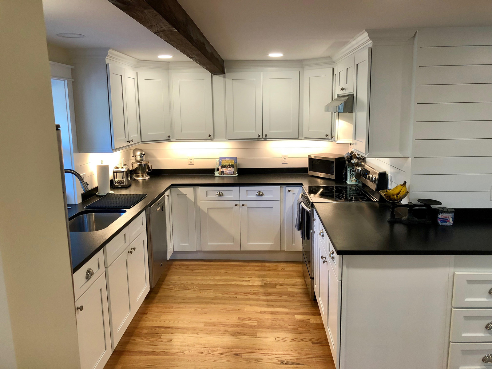 Remodeled kitchen with white shaker cabinets, black counters and an exposed beam