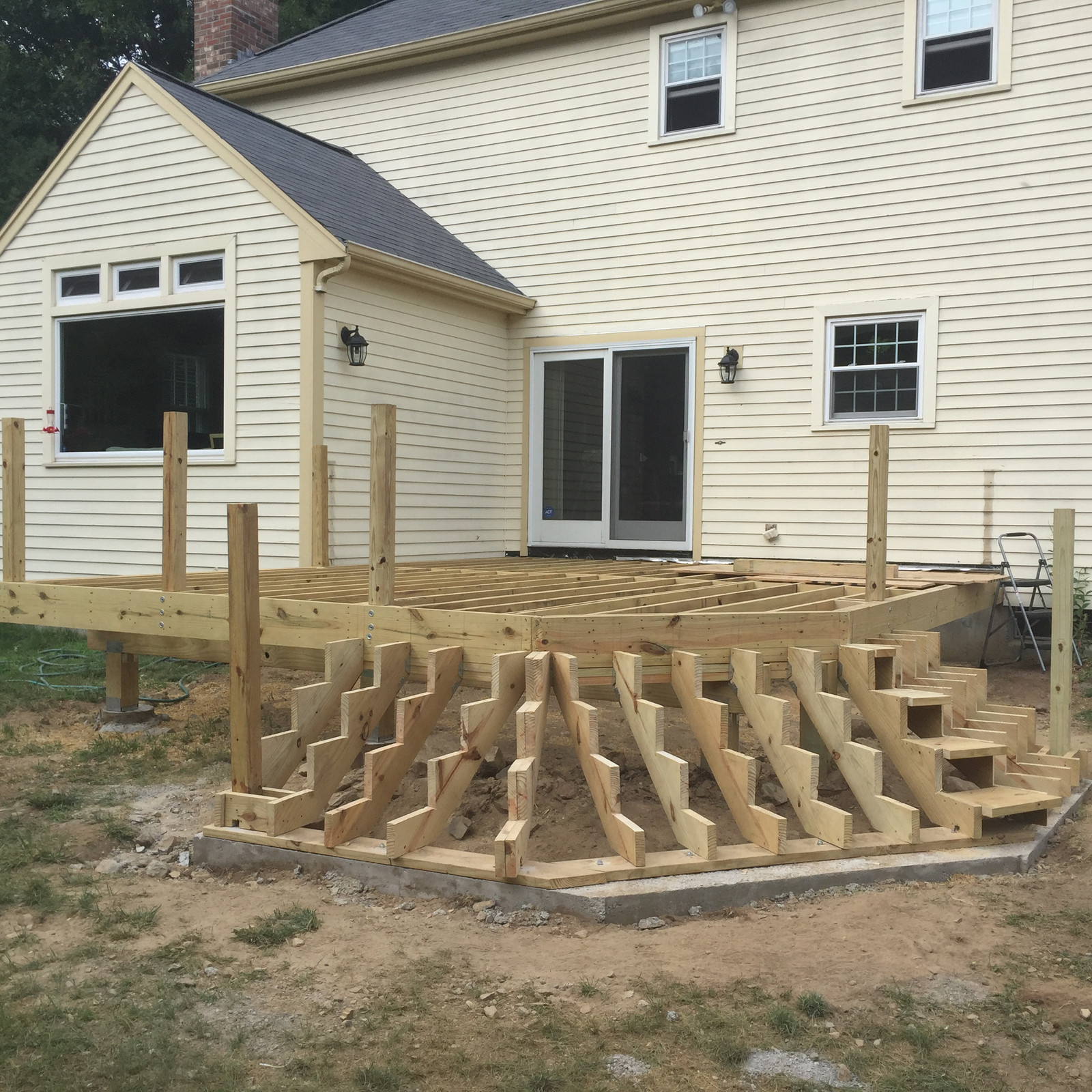 Deck framing with curved stair stringers against a cream clapboard house