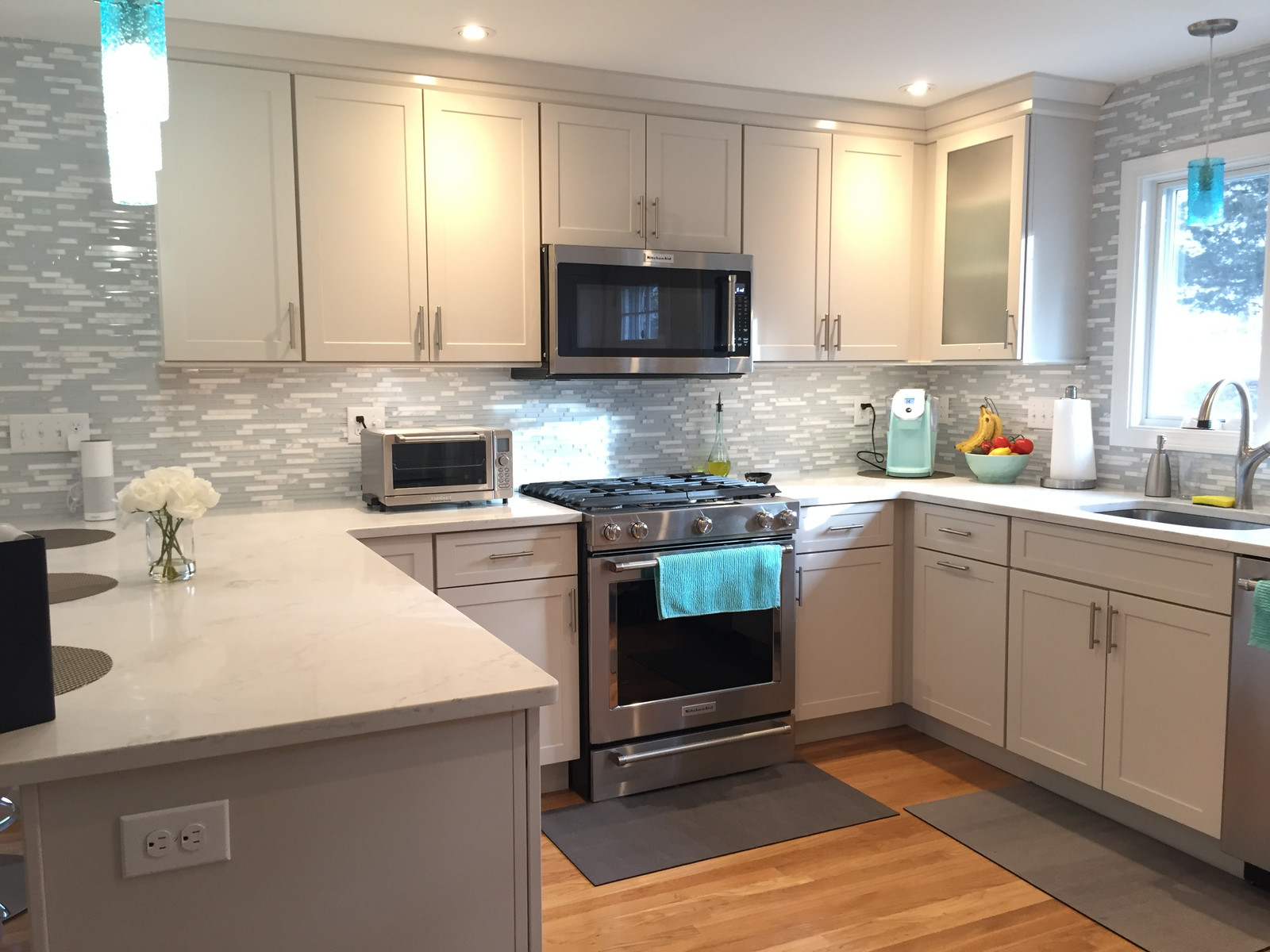 Kitchen with light grey shaker cabinets, glass tile backsplash and quartz counters