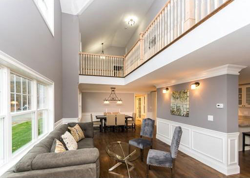 Open living and dining room with a second floor balcony rail, wainscoting, a chandelier and hardwood floors