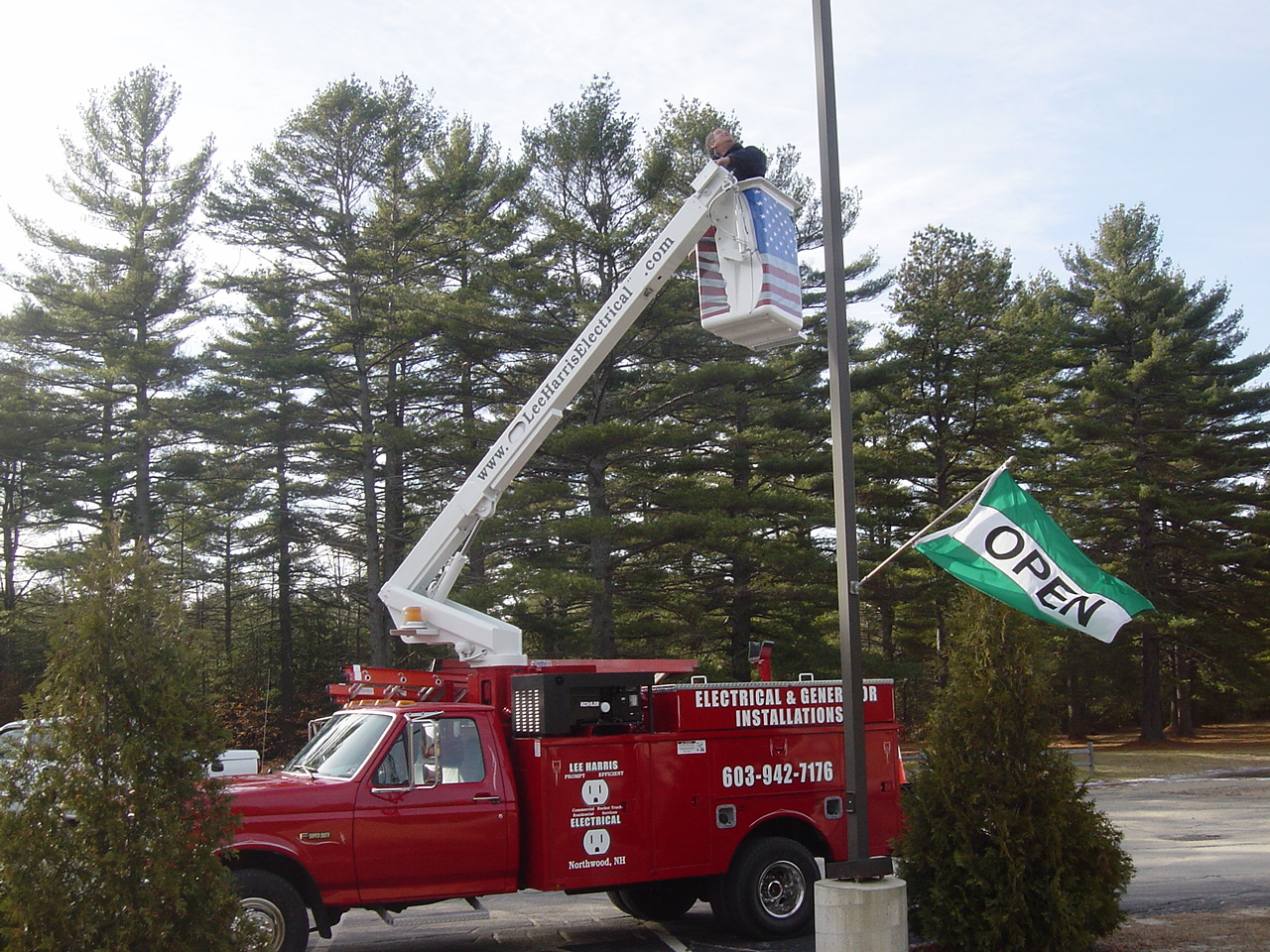 Lee Harris Electrical bucket truck with the boom raised beside a roadside sign pole, an electrician working from the bucket.