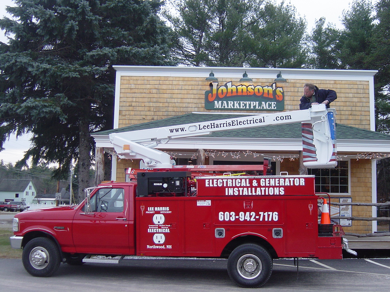 The red bucket truck parked outside Johnson's Marketplace with the boom reaching over the storefront roof.