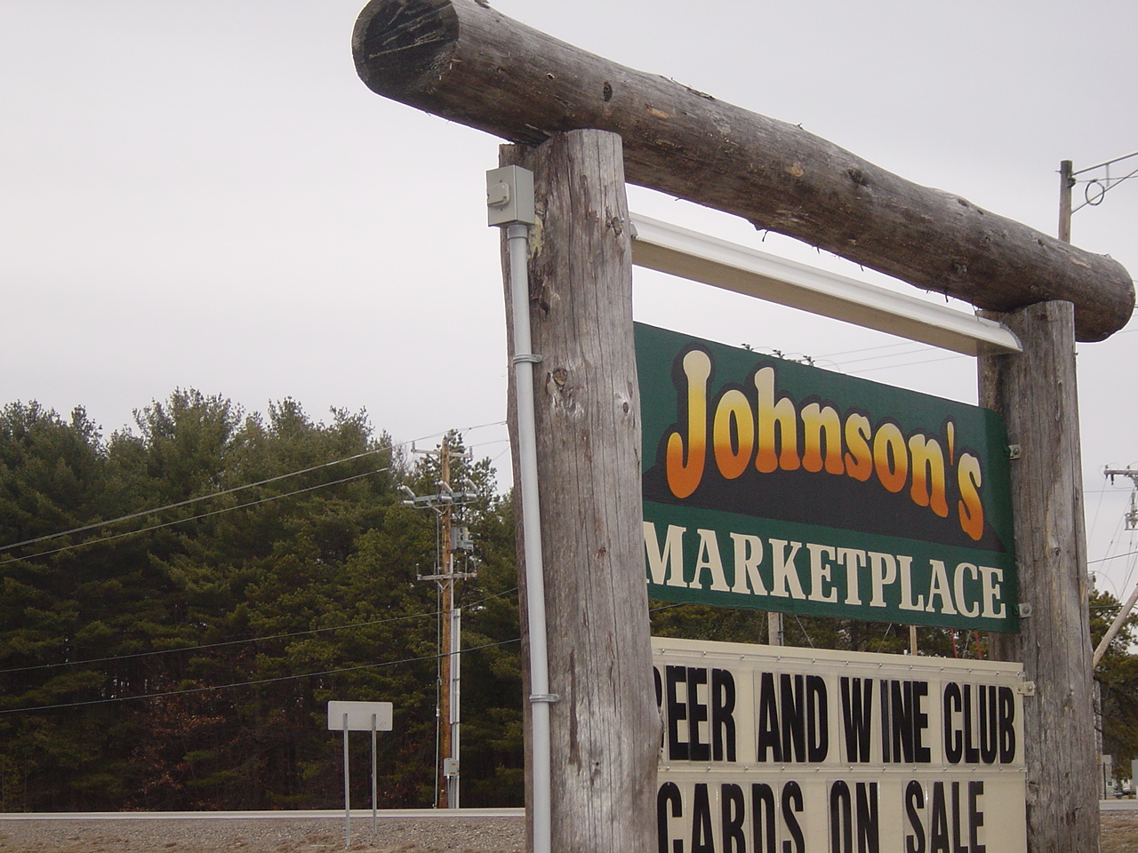 The log-post roadside sign for Johnson's Marketplace, with a light fixture mounted above it.