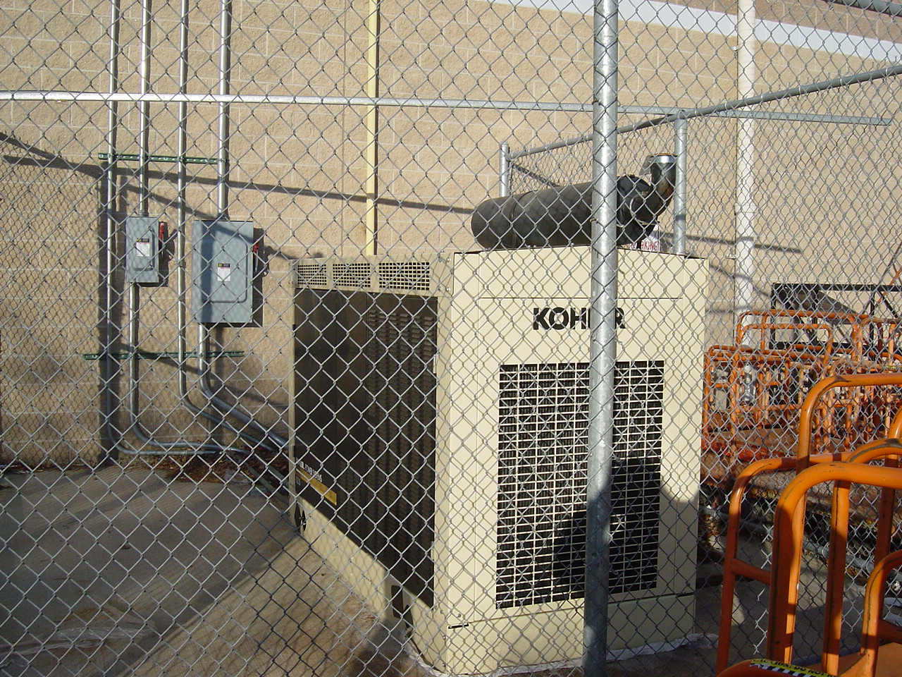 A pair of Kohler standby generators inside a chain-link enclosure.