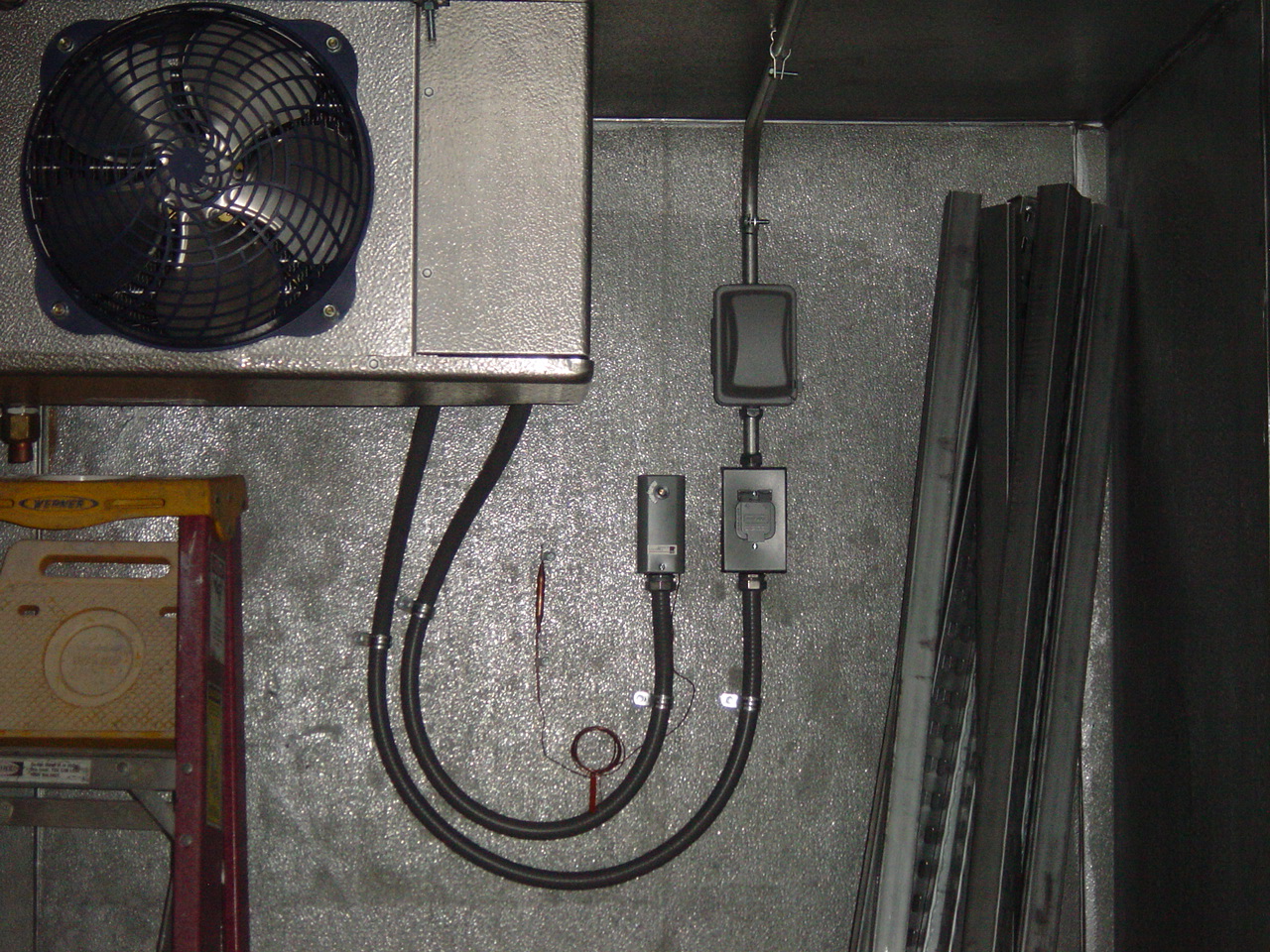 A walk-in cooler condenser and its disconnect mounted on a stainless wall.