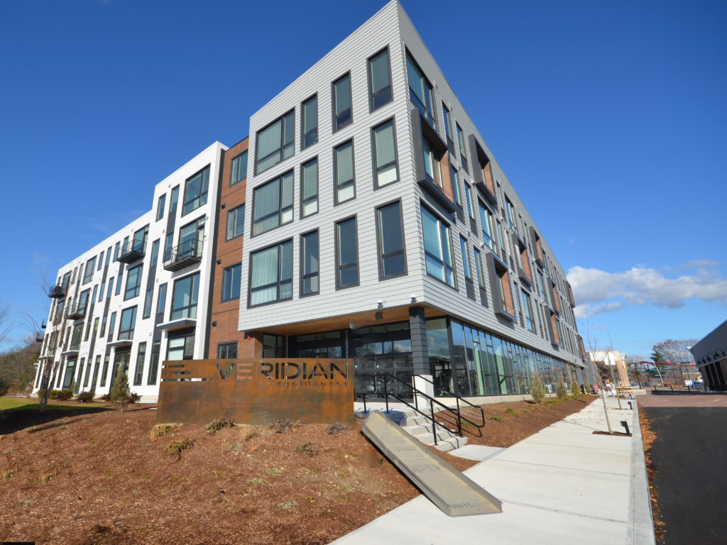 A five-story residential building with a corten steel sign at the entry walk.