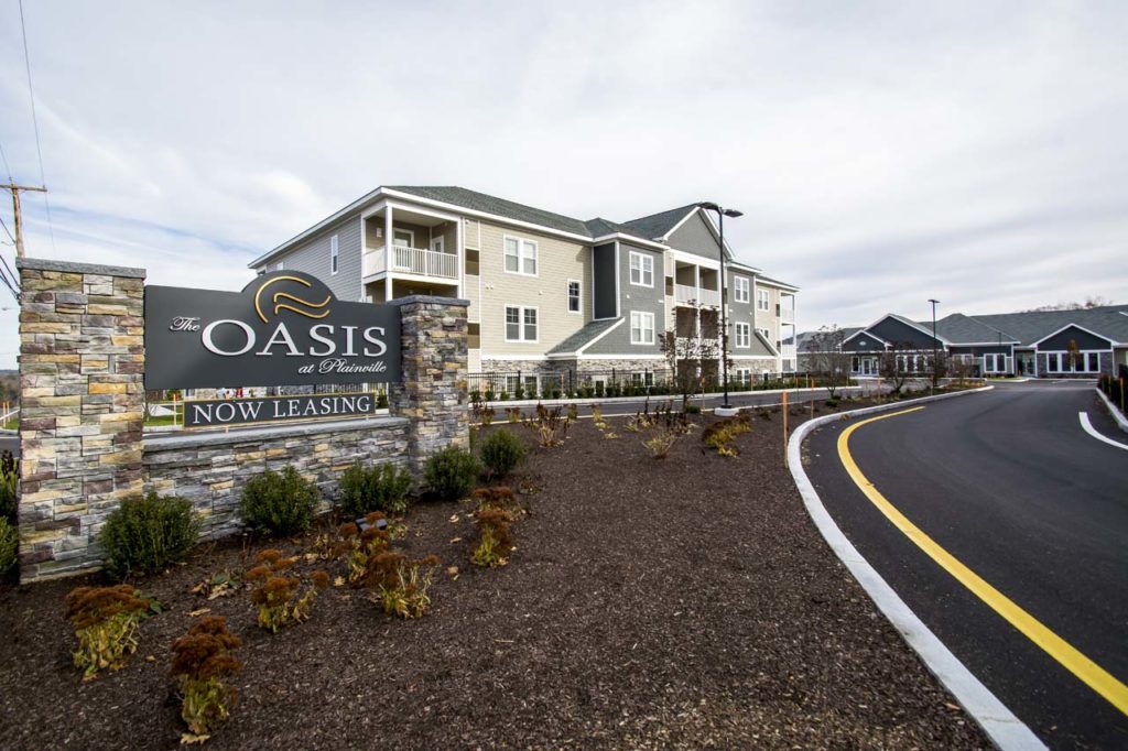 A stone-piered entrance sign in front of a finished three-story residential community.