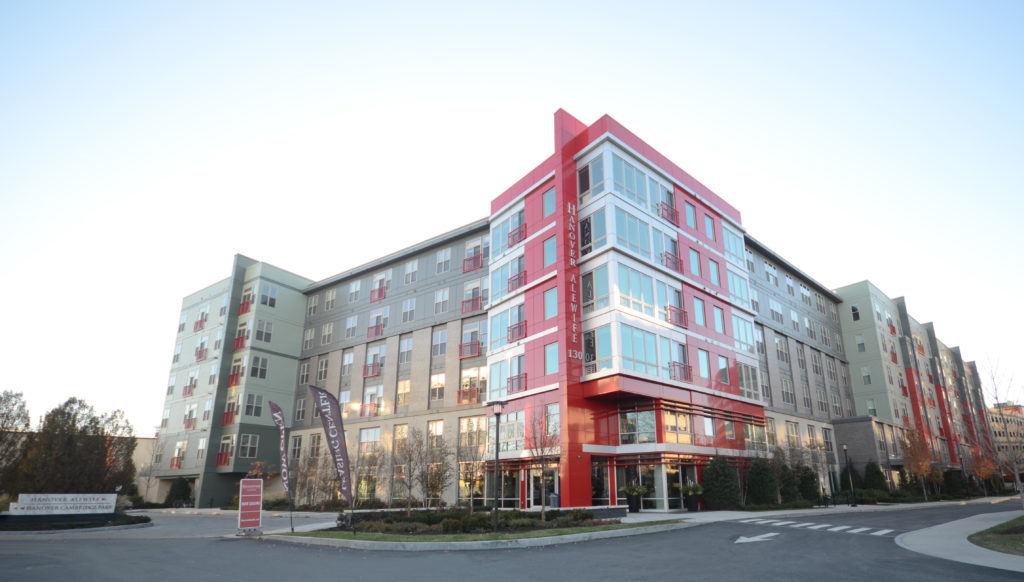 A large red and grey apartment block at dusk with a lit lobby entrance.