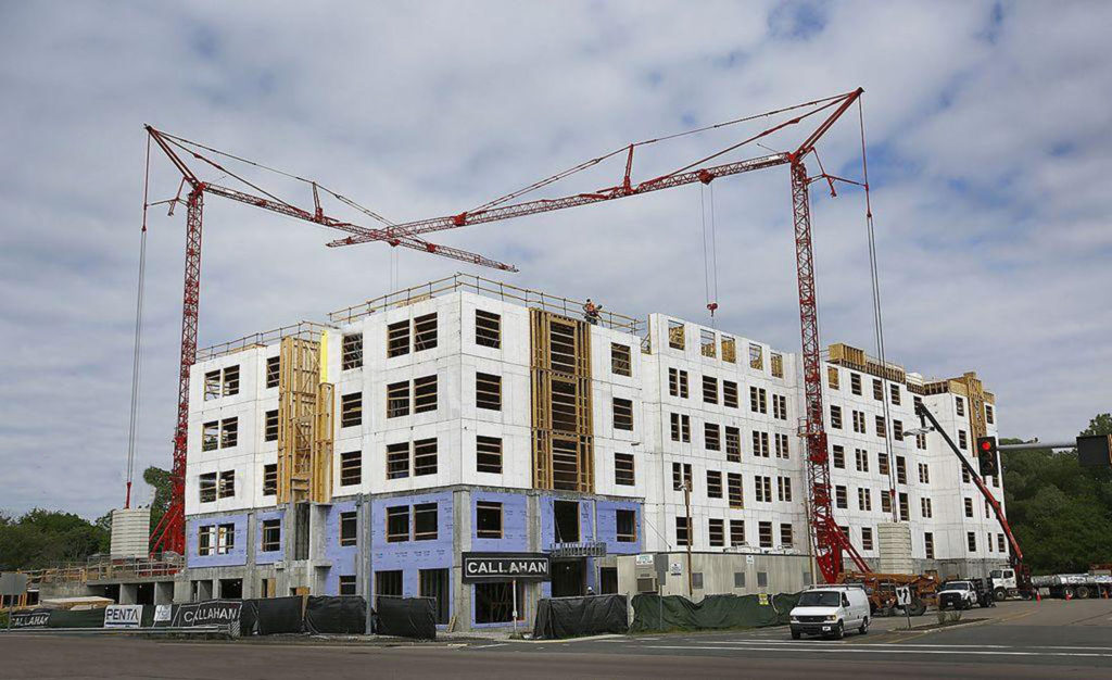 Two tower cranes over a mid-rise building under construction, concrete decks and framing exposed.