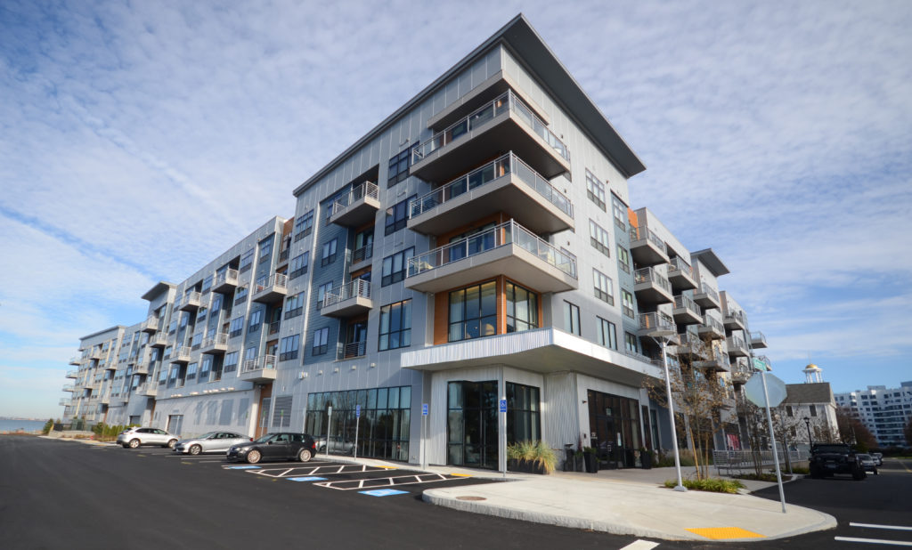 A finished waterfront apartment building with stacked balconies, parking lot striped and open.