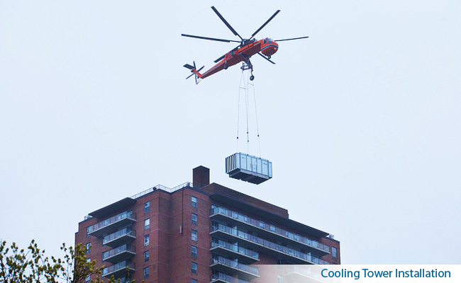 A heavy-lift helicopter setting a cooling tower onto the roof of a high-rise.