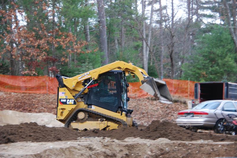 A CAT 259D compact track loader moving earth on a cleared lot behind orange safety fence