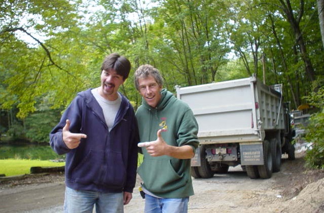 Two men standing beside a dump truck on a wooded job site