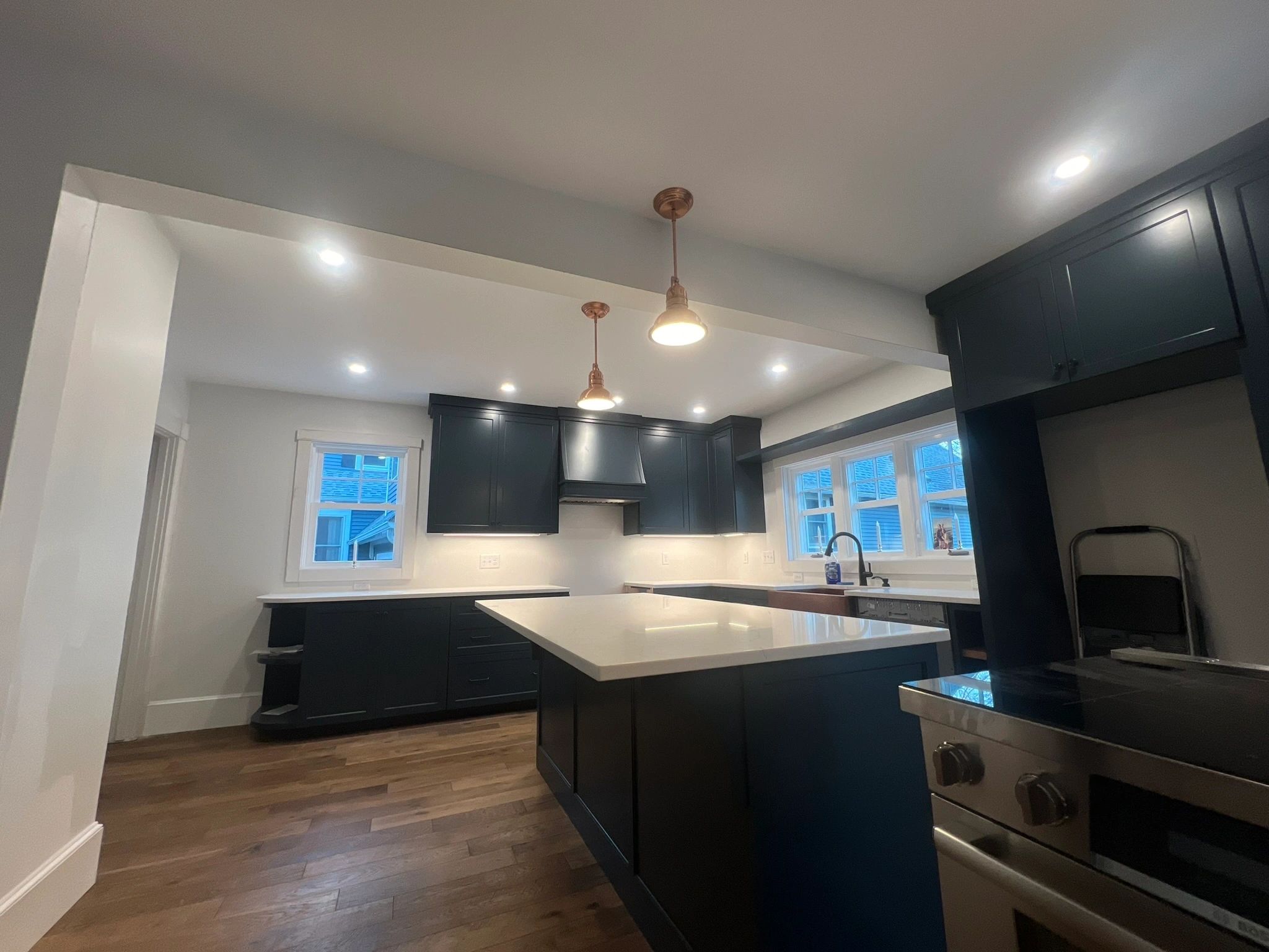 A finished kitchen with dark cabinetry, a large island, warm pendant lights and recessed ceiling lights