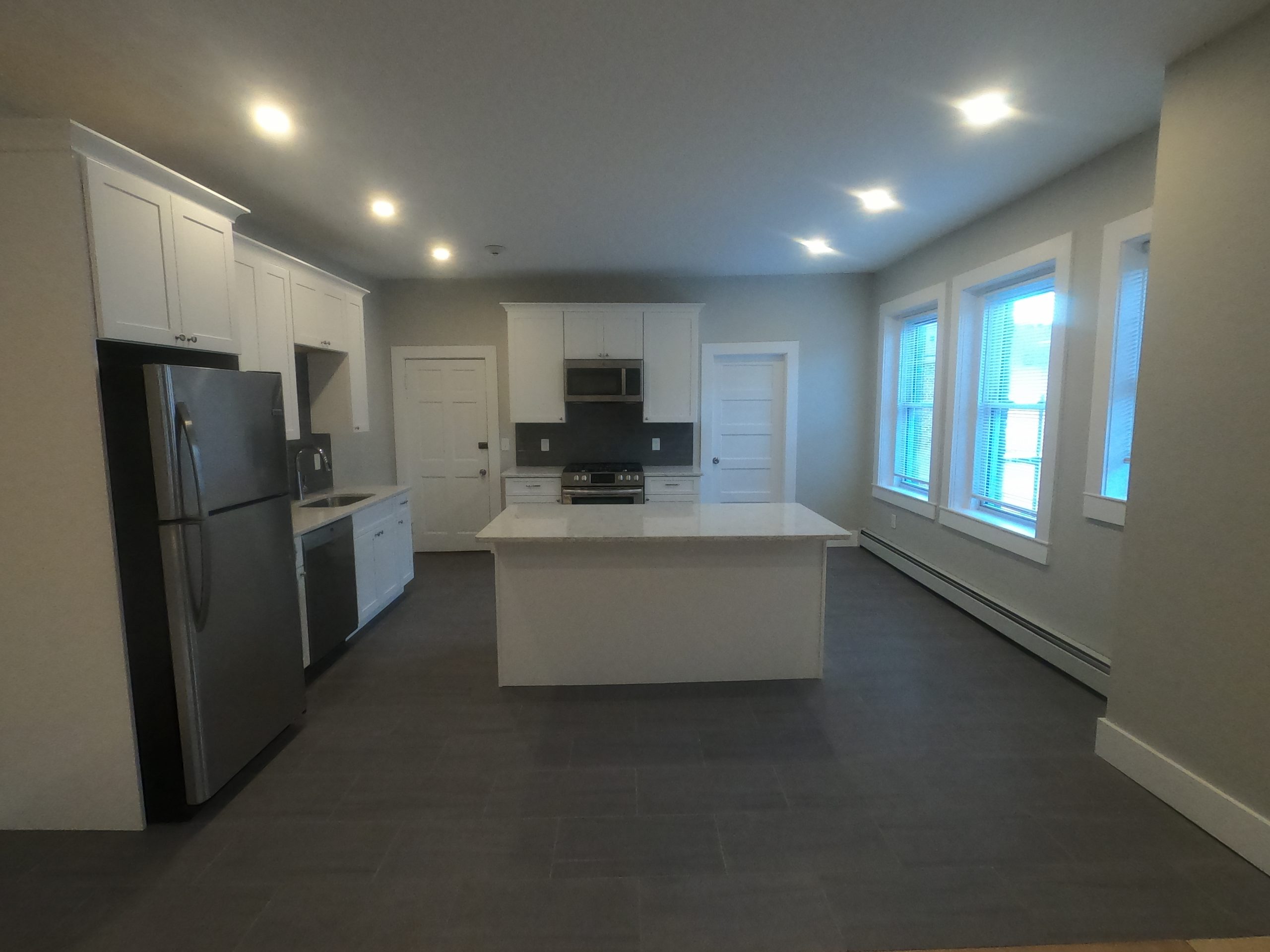 Finished open kitchen with white shaker cabinets, a quartz island and large tile floor