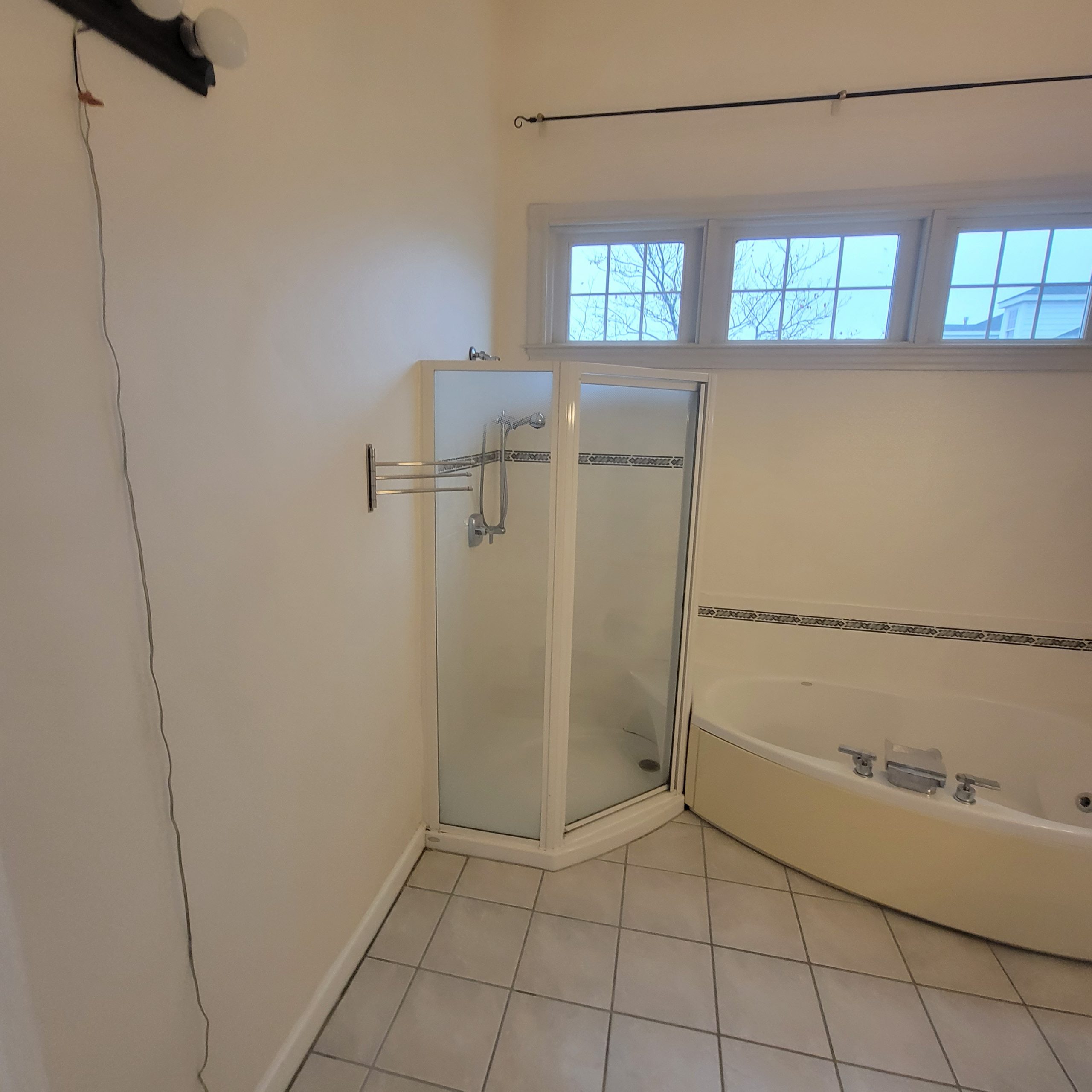 Dated bathroom before work, with a corner shower stall, a built in corner tub and white floor tile