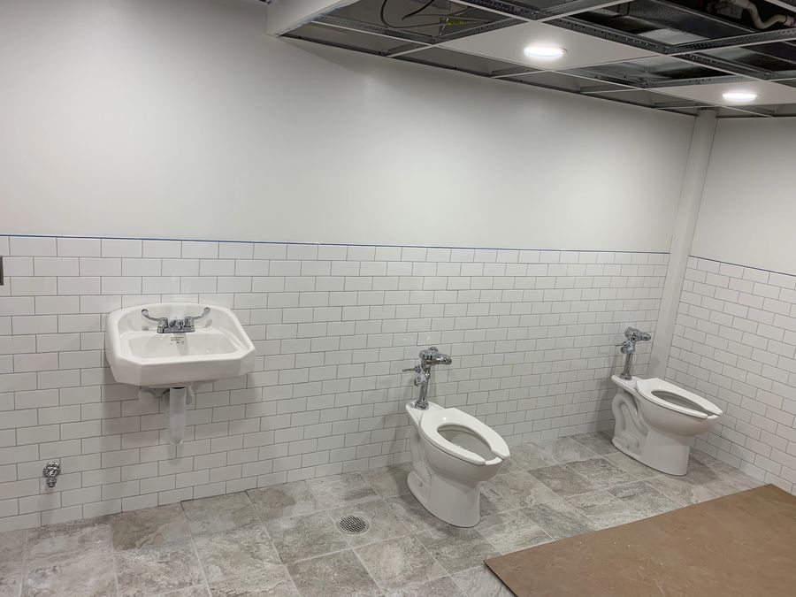 Commercial restroom with a wall hung sink and floor mounted toilets set in white subway tile