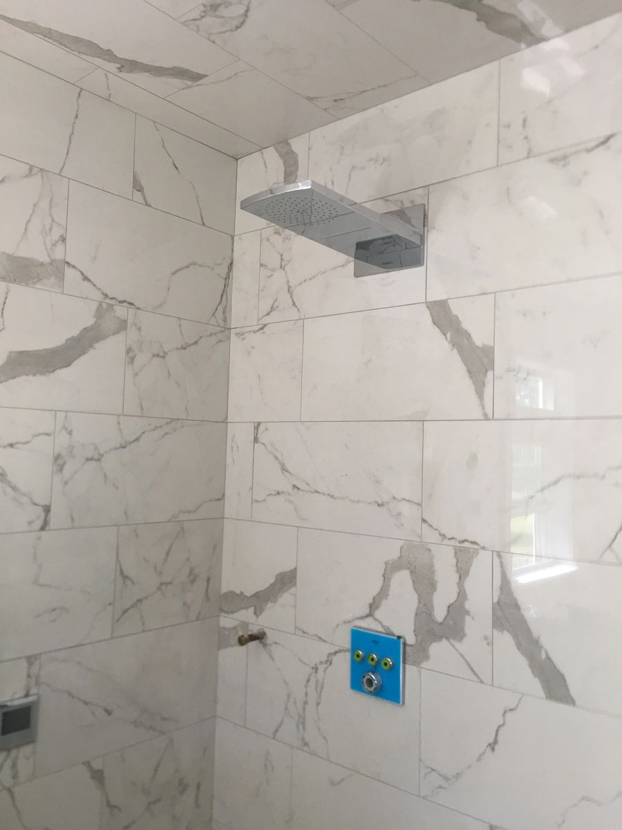 Marble look tile shower wall with the rain head hung and the valve rough-in still guarded