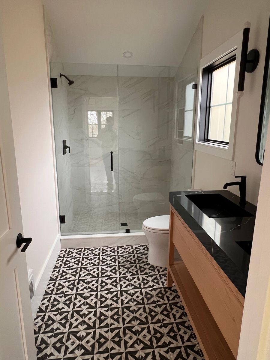 Glass shower enclosure beside a black and white patterned tile floor and a dark stone vanity top