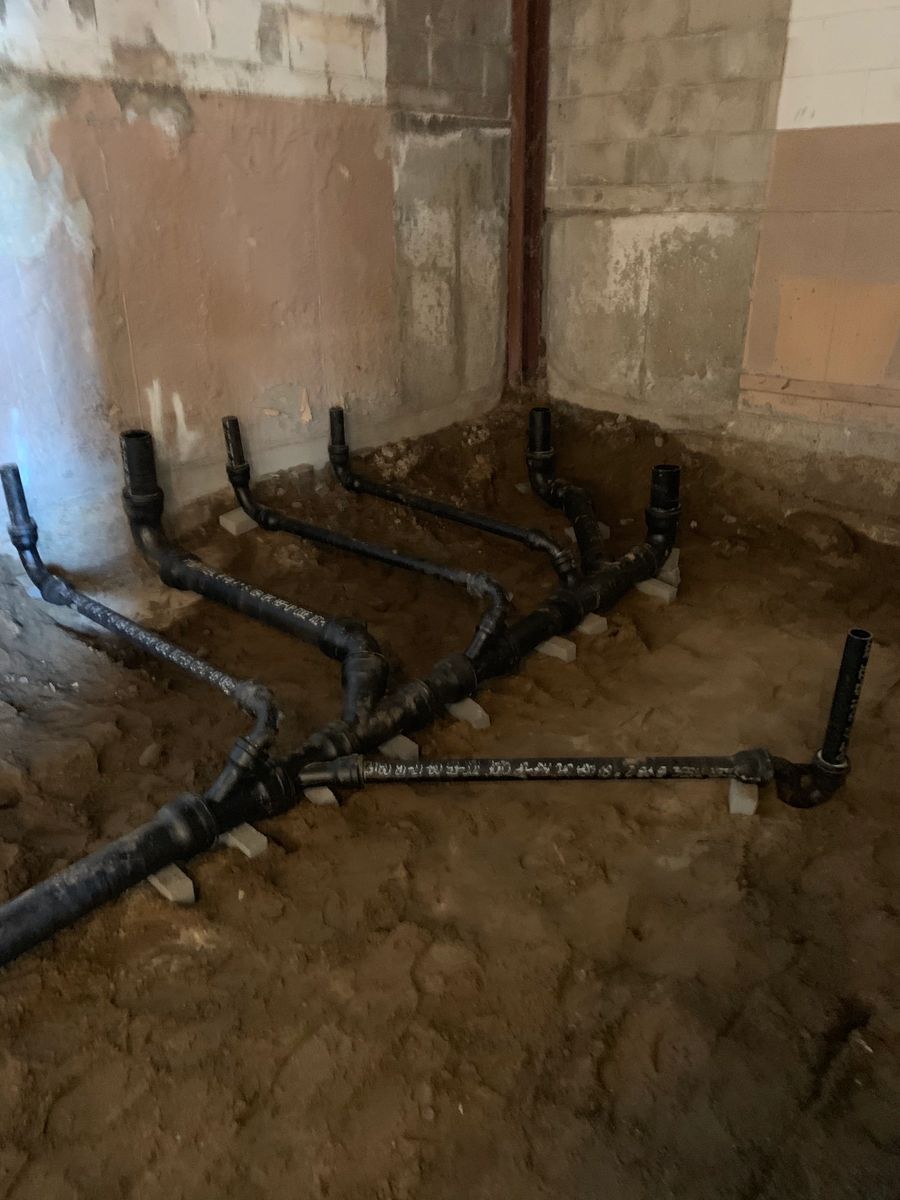 Drain lines run under a basement floor against an old stone foundation wall