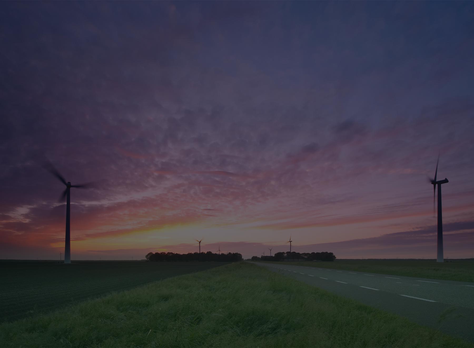 Wind turbines standing over a road at sunset