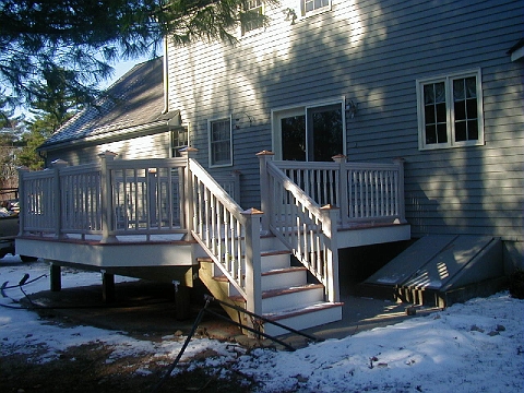 Deck with a white rail and stairs down to the yard, on grey clapboard siding