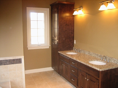 Double vanity in dark wood cabinetry with a tall linen cabinet alongside