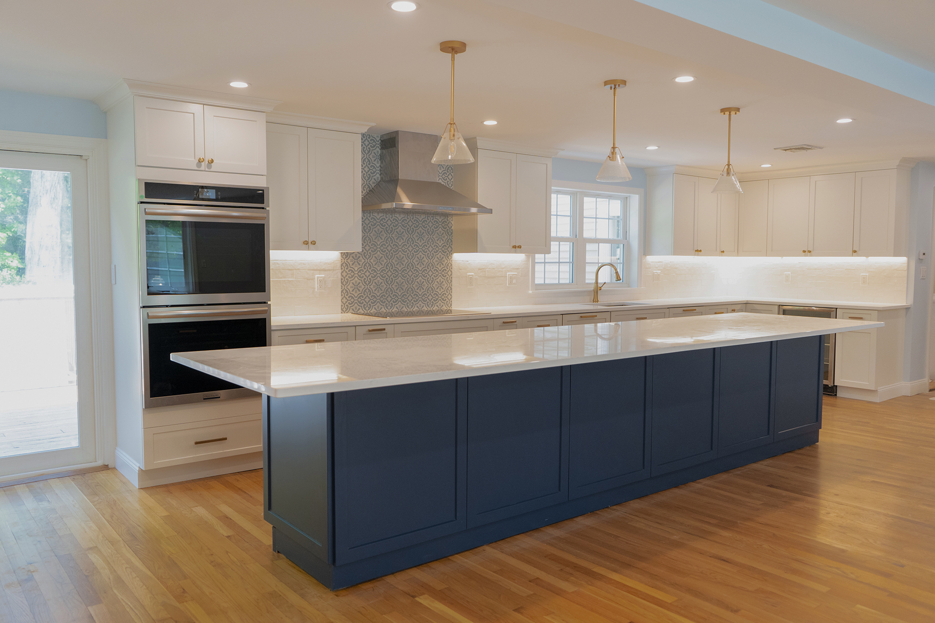 Finished white kitchen with a deep navy island, marble counter, brass pendant lights and wide plank oak floors