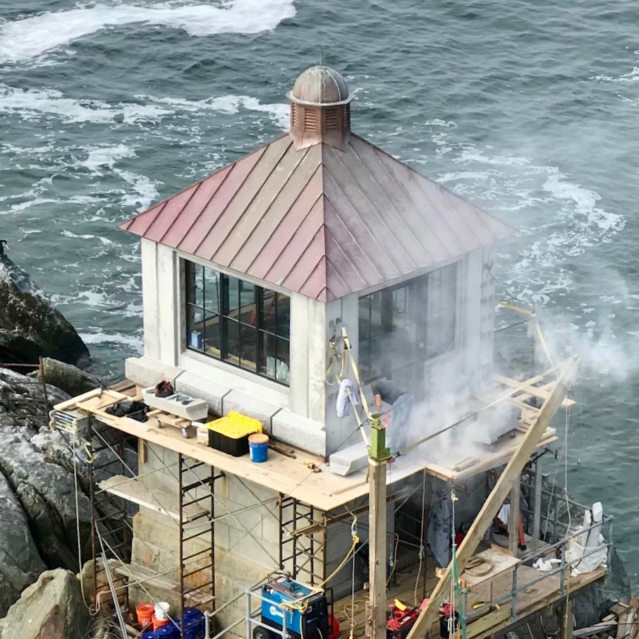 An offshore lighthouse standing on a bare rock ledge in open surf, wrapped in staging
