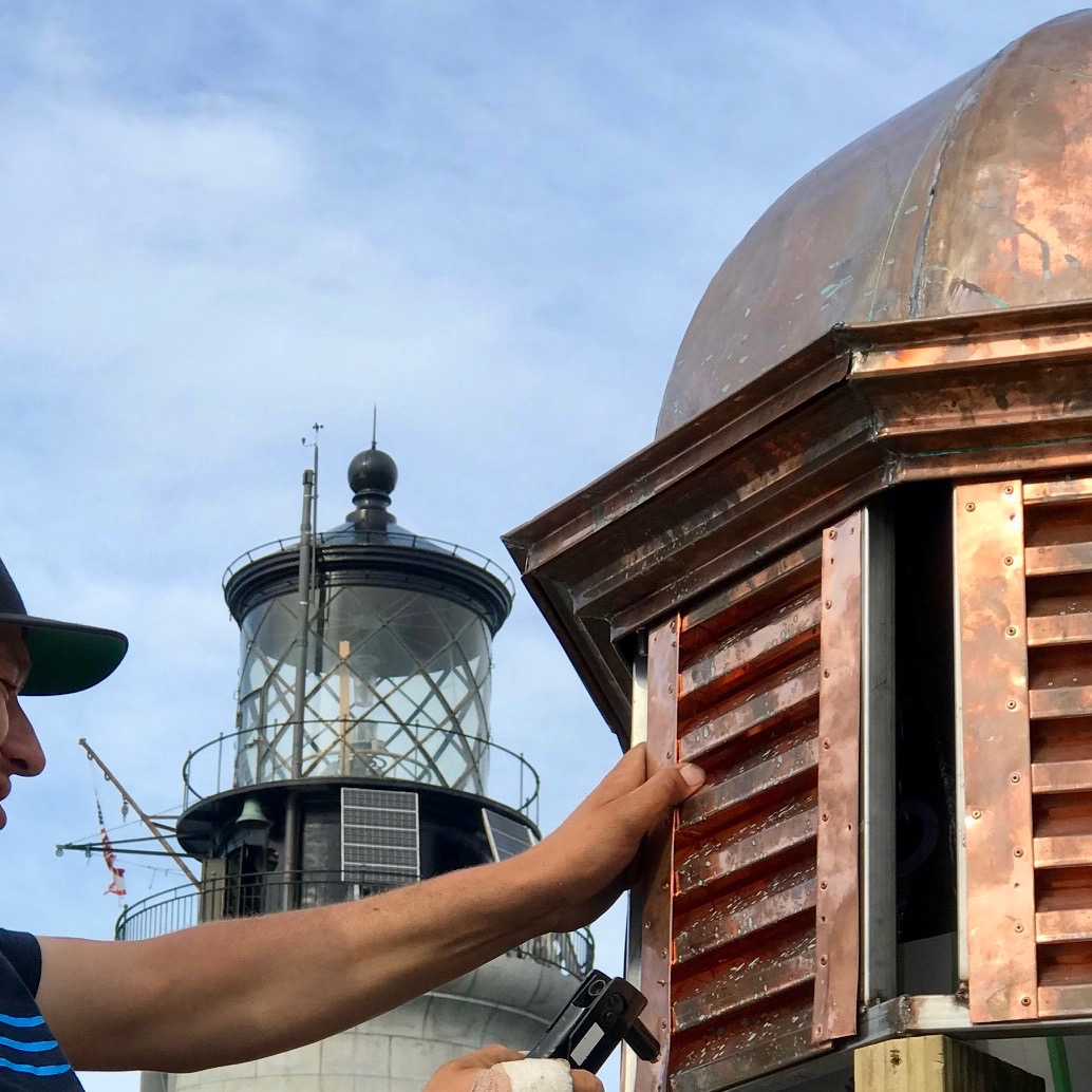 A man working by hand on the copper clad lantern room of a lighthouse