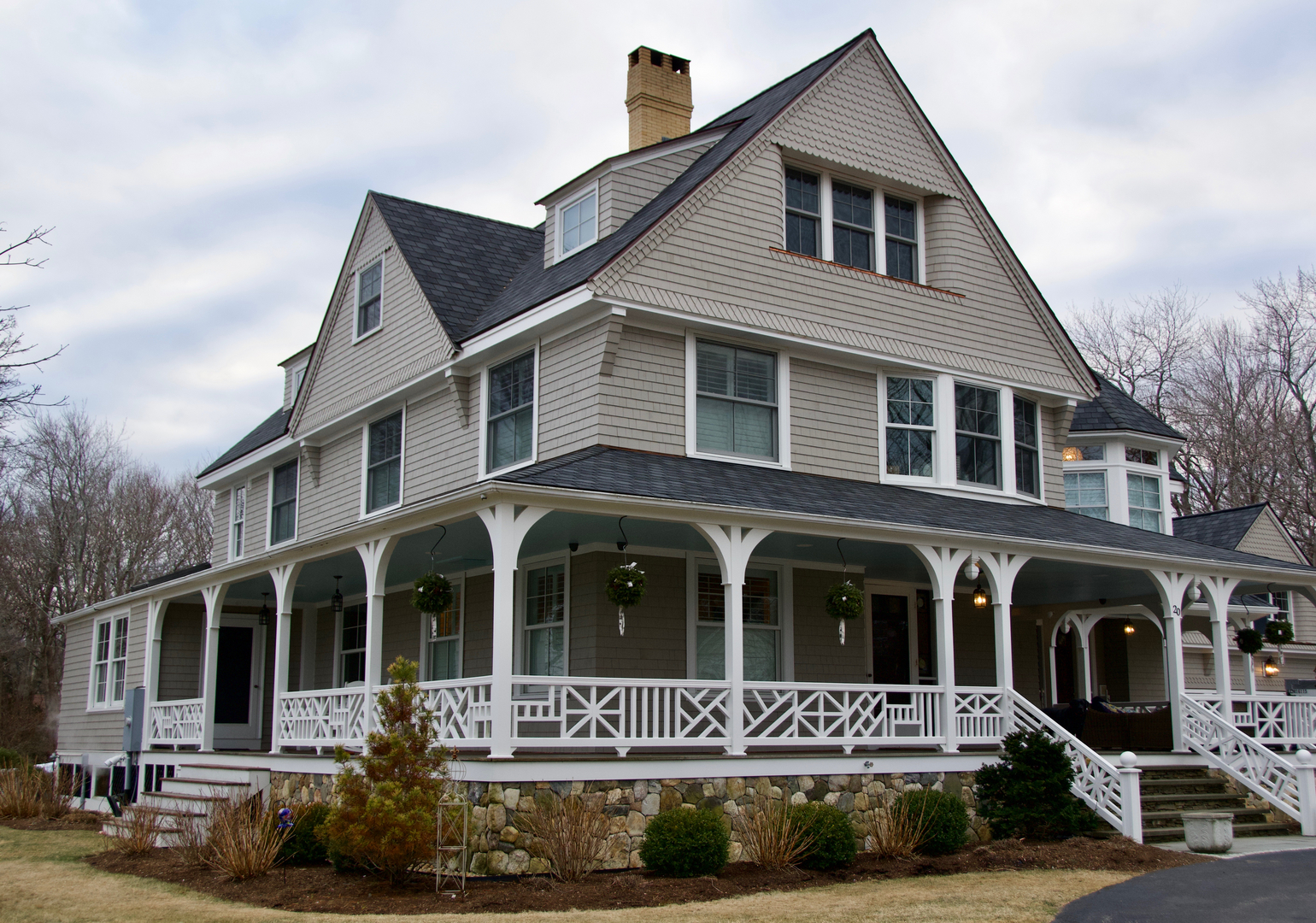 A large shingle style Victorian with a deep wraparound porch, lattice railings and granite steps