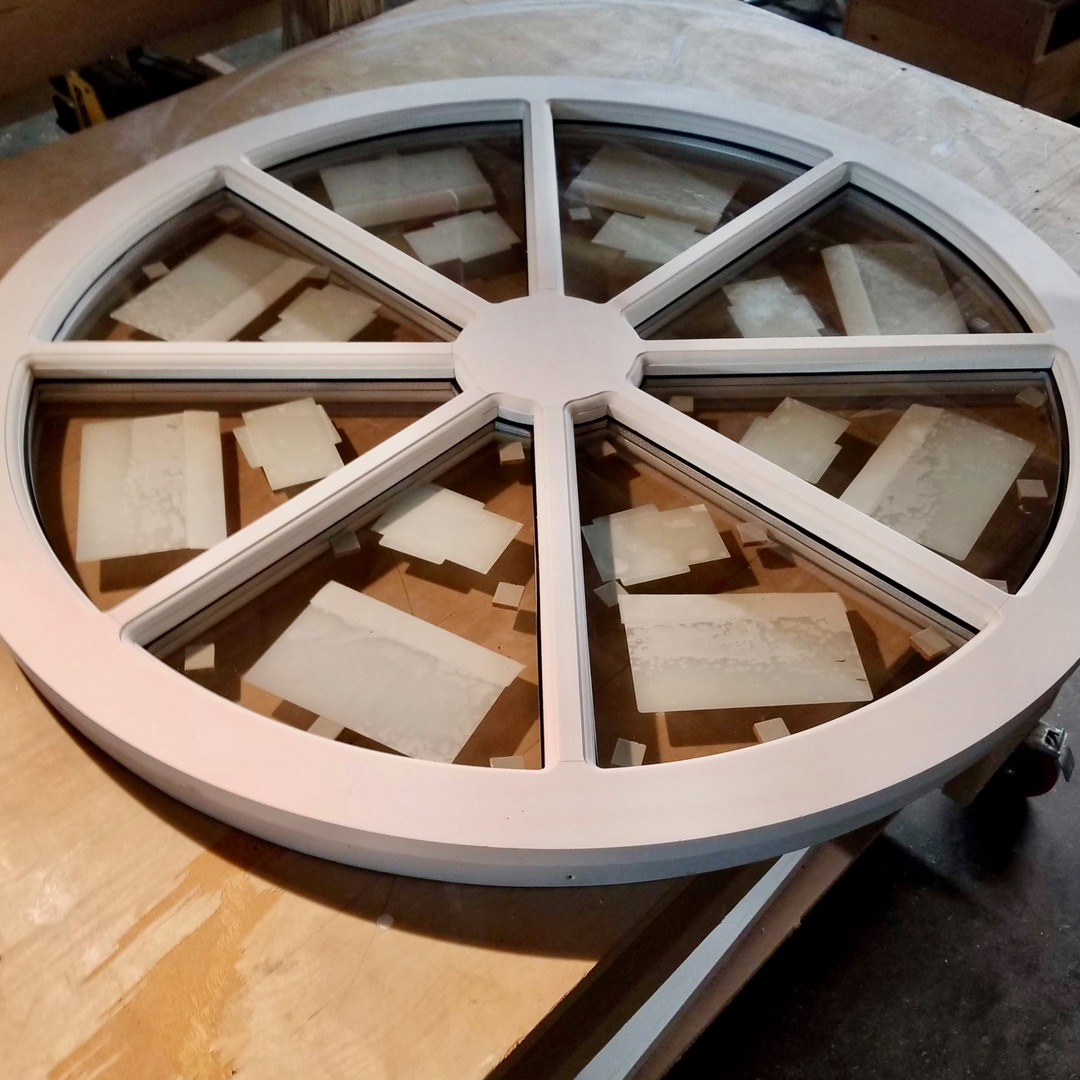 A large round wheel spoke window sash under construction on the bench