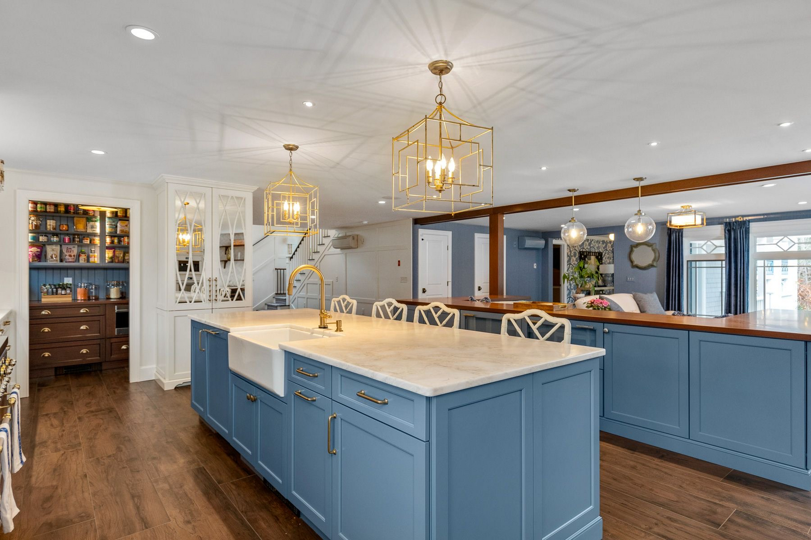 A high end kitchen with a soft blue island, brass lantern pendants and white perimeter cabinetry