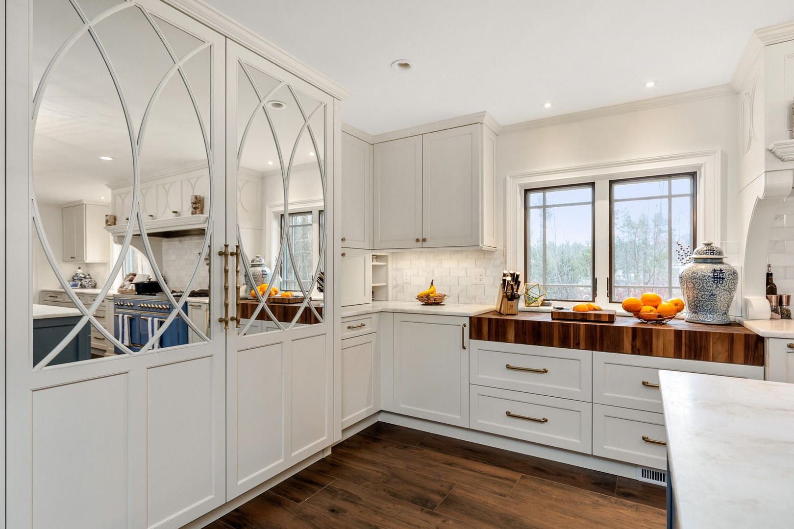 A white kitchen with gothic arched glass cabinetry and a wood counter run