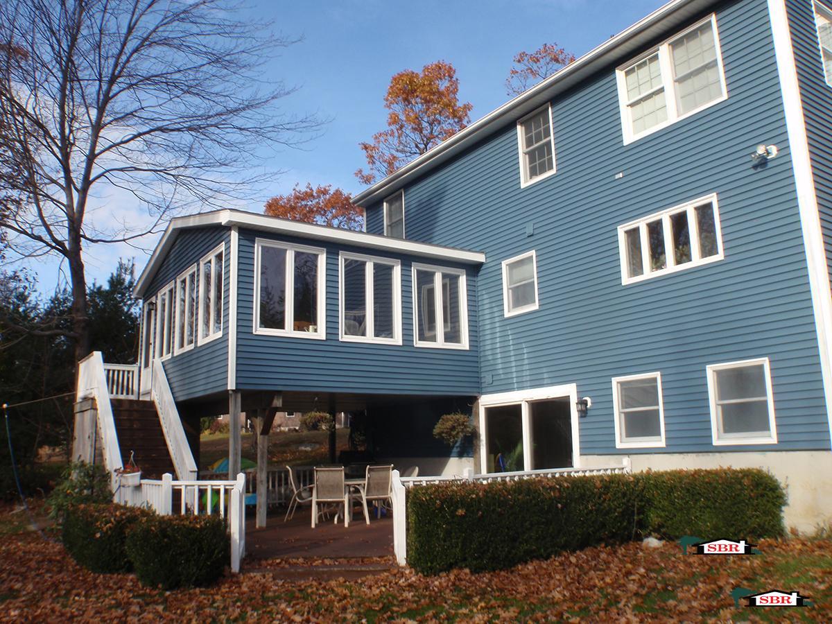 Blue colonial with a raised sunroom addition over a covered patio