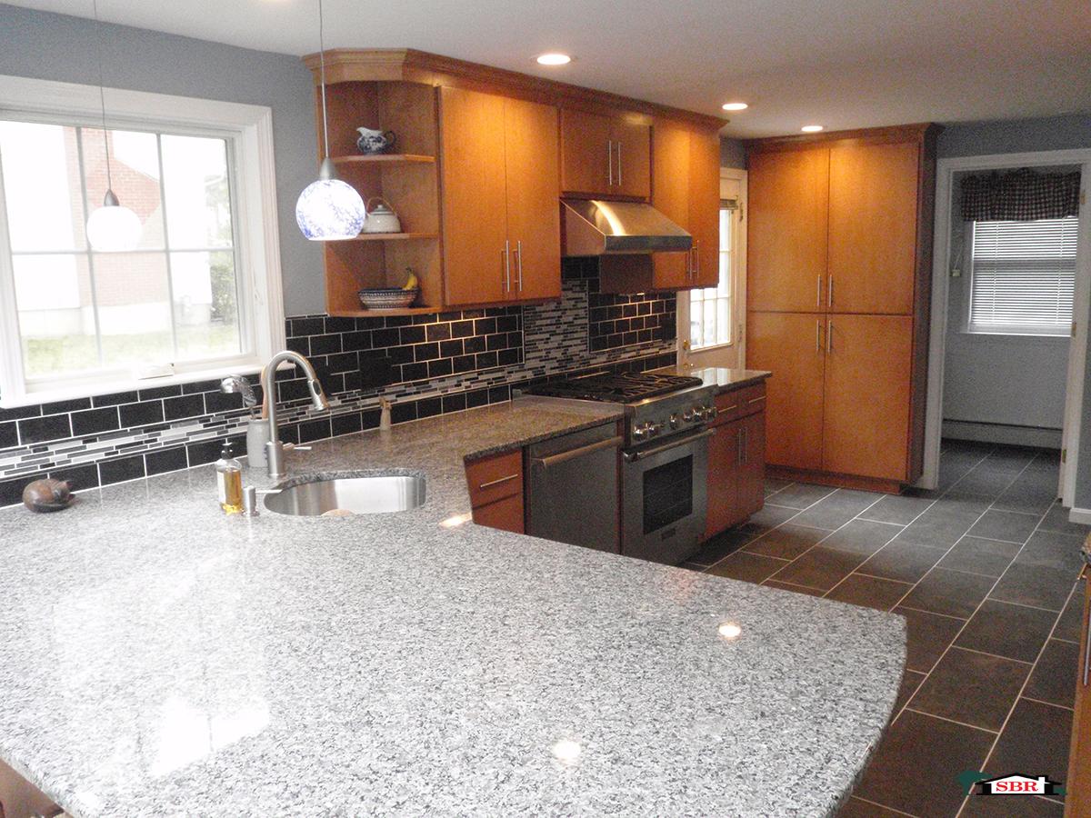 Kitchen with granite peninsula, black glass backsplash and maple cabinets