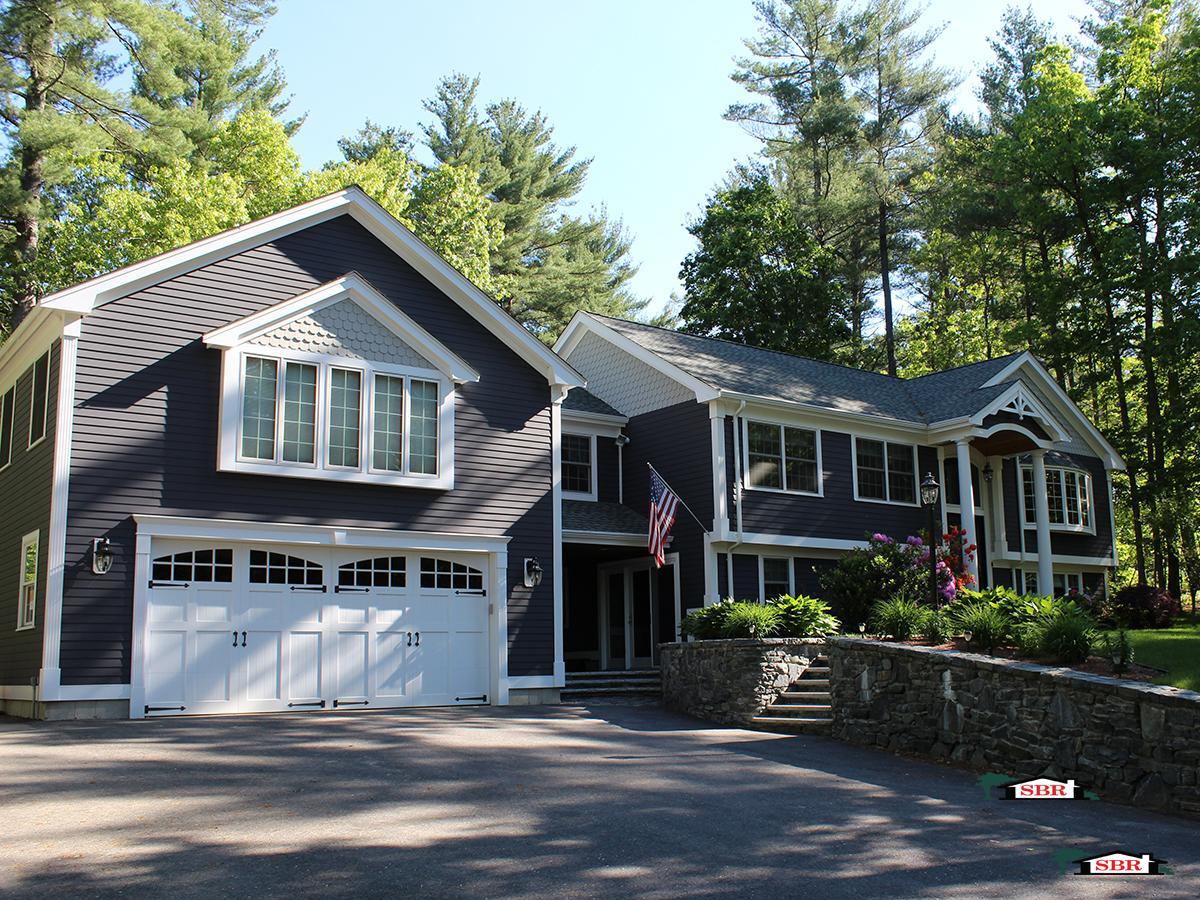 The same raised ranch after: blue siding, a garage wing, new roof, columned entry and a stone wall
