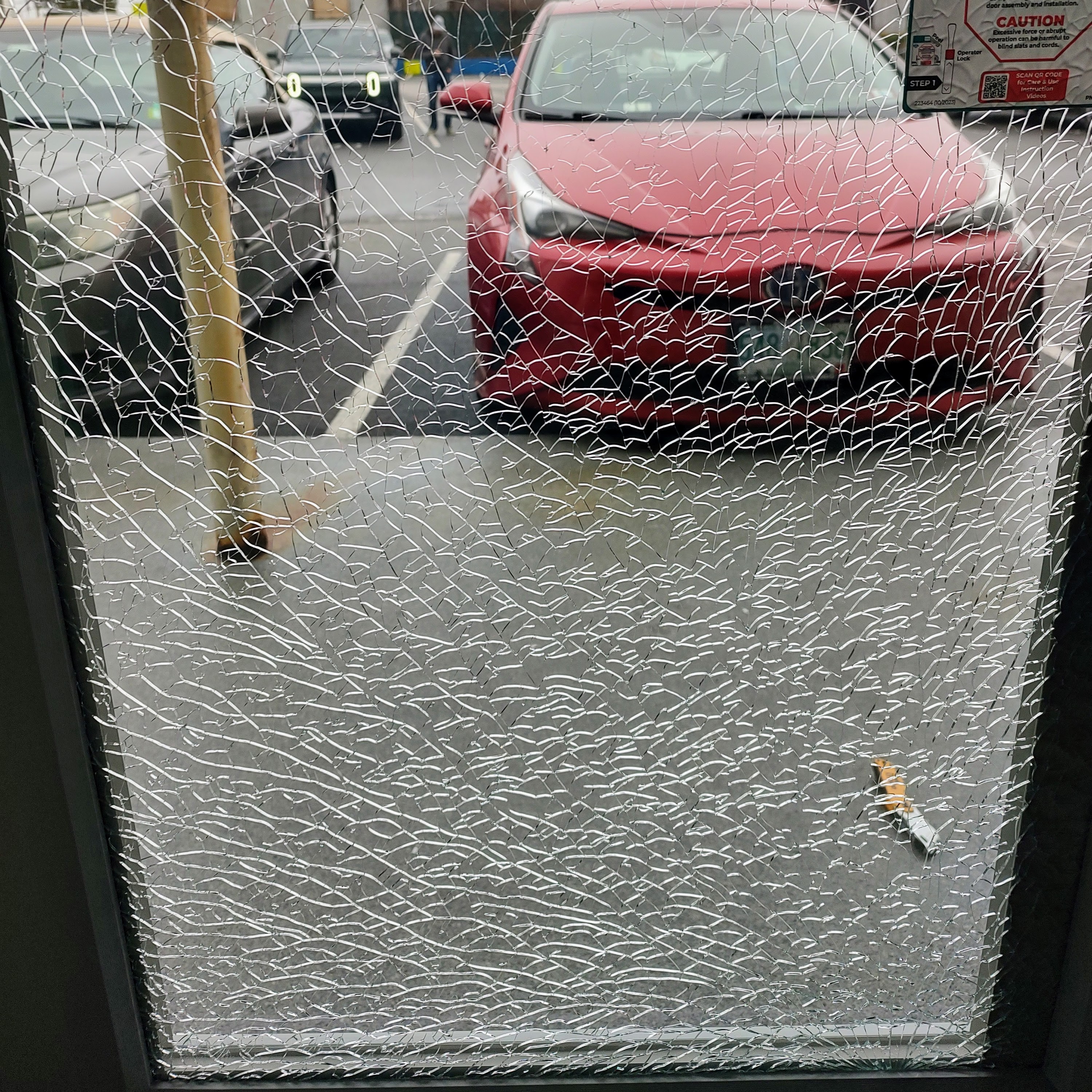 A pane of tempered safety glass shattered into a web of small pieces, with a parked car visible behind it