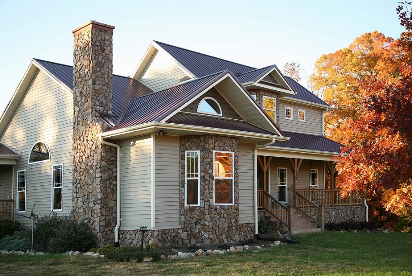 Finished home exterior with a stone chimney, seamless metal roof and new siding