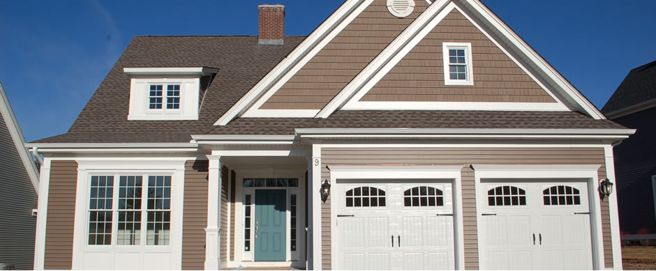 Taupe shake and clapboard siding with white trim, a teal front door and two white garage bays under a deep blue sky