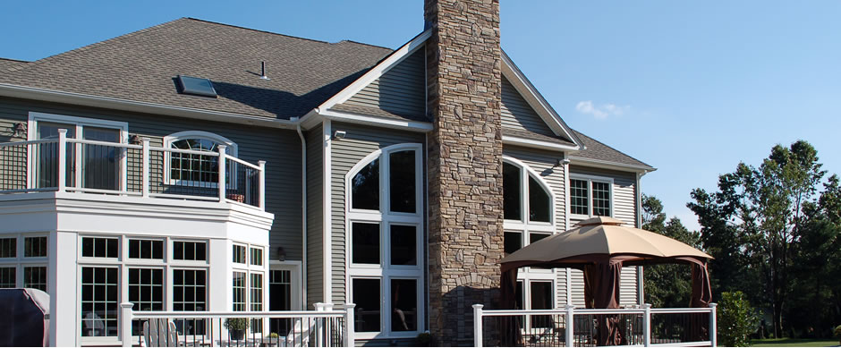 Large house with a stone chimney, a glass gable and a railed rear deck