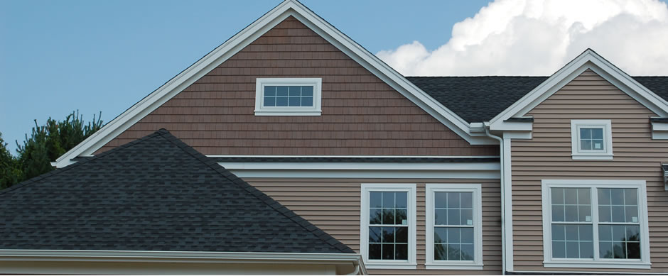 Brown shake gable and asphalt roof shingles meeting white trim against a clear sky
