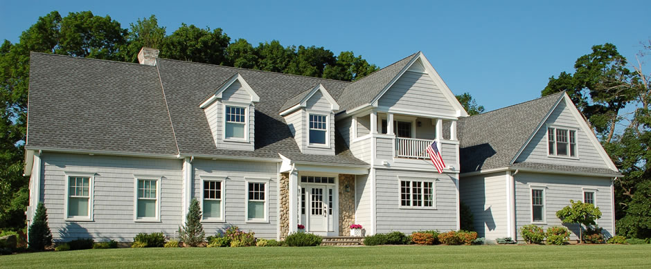 Gray cape with dormers and a flag on a wide green lawn