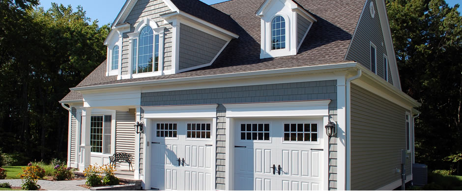 Blue gray shingled house with dormers and white carriage style garage doors