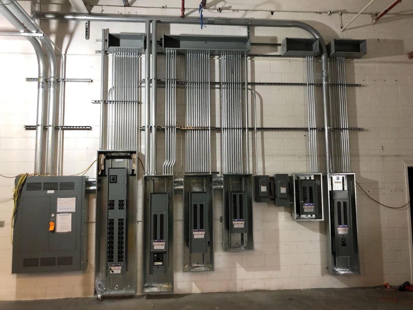 A bank of eight panelboards on a block wall with racked conduit sweeping into the ceiling